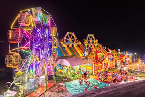 Illuminated Ferris wheel, bouncing castle and carousel at night in a funfair in Vientiane, Laos.jpg